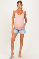 woman wearing a pink maternity tank top and denim shorts, holding her baby bump