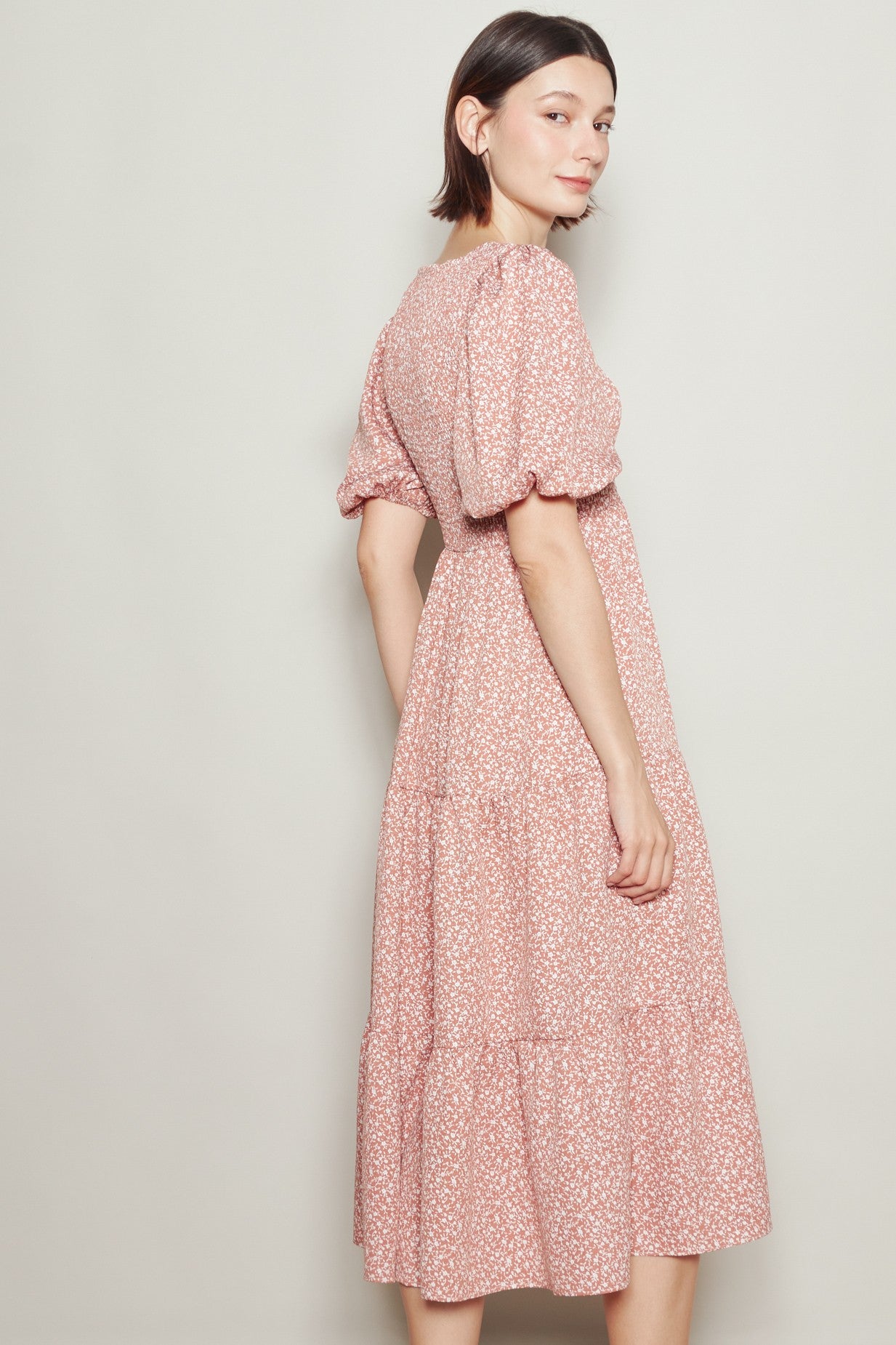 woman wearing a pink floral print midi dress with puff sleeves and a tiered skirt, posed from the back