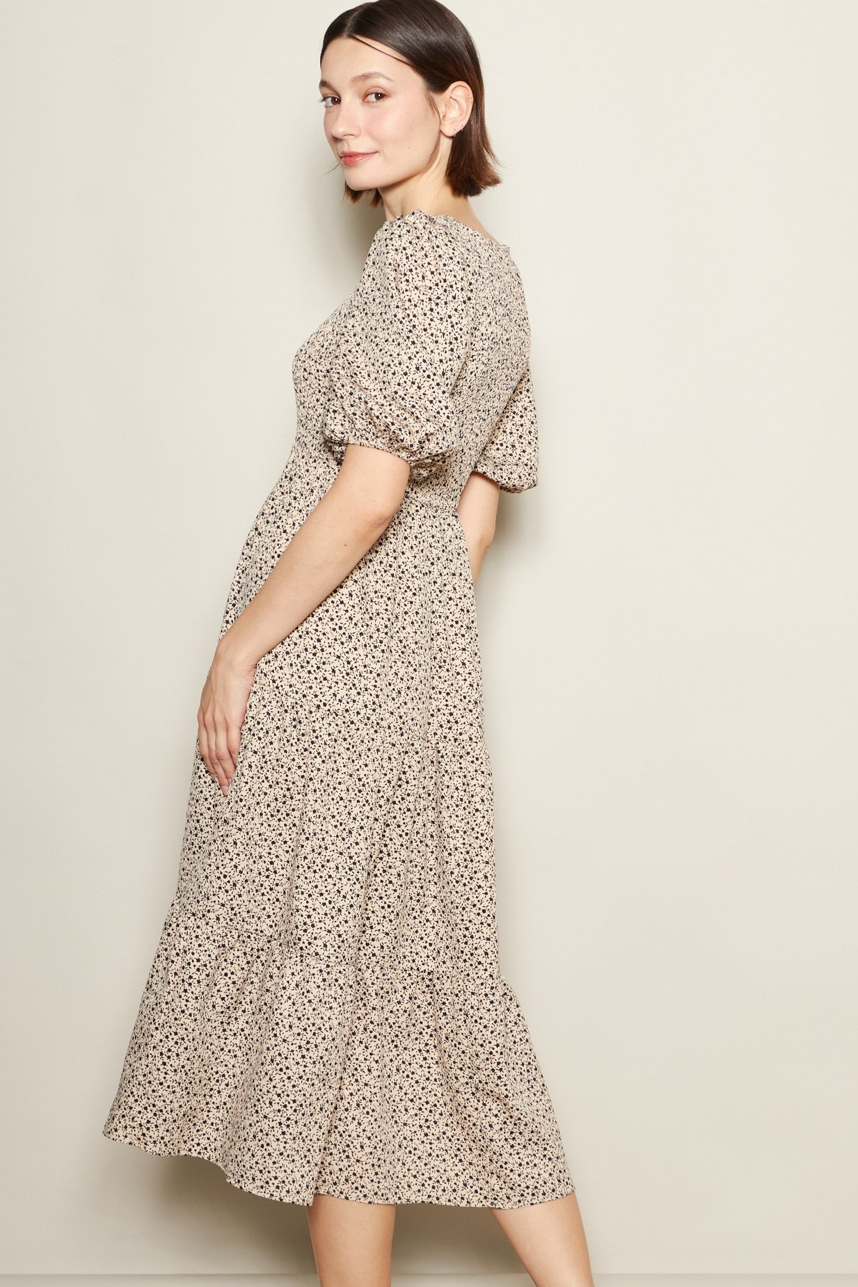 woman wearing a beige floral midi dress with puff sleeves and a tiered skirt, posed sideways against a neutral background