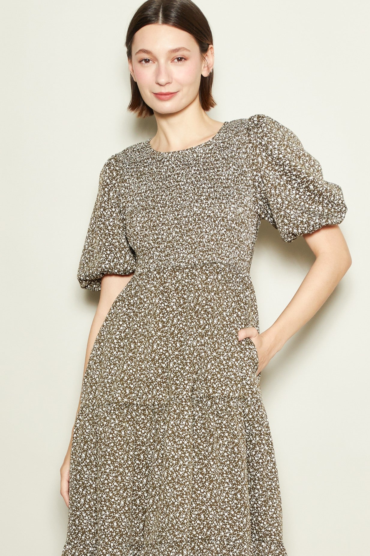 woman wearing a brown floral print midi dress with puff sleeves and a fitted waist, smiling at the camera