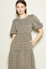 woman wearing a brown floral print midi dress with puff sleeves and a fitted waist, smiling at the camera