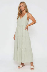 woman wearing a light green striped maxi dress with a v-neck and tiered skirt, standing sideways with hands in pockets