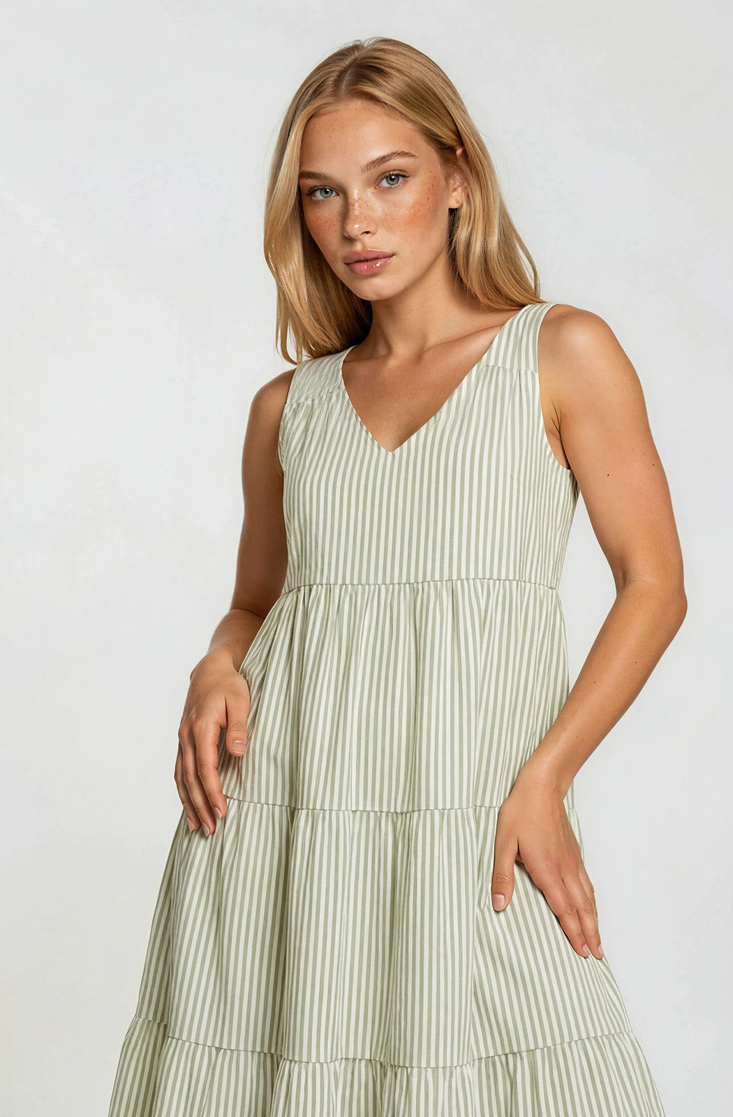 woman wearing a light green striped sleeveless tiered dress with a v-neckline