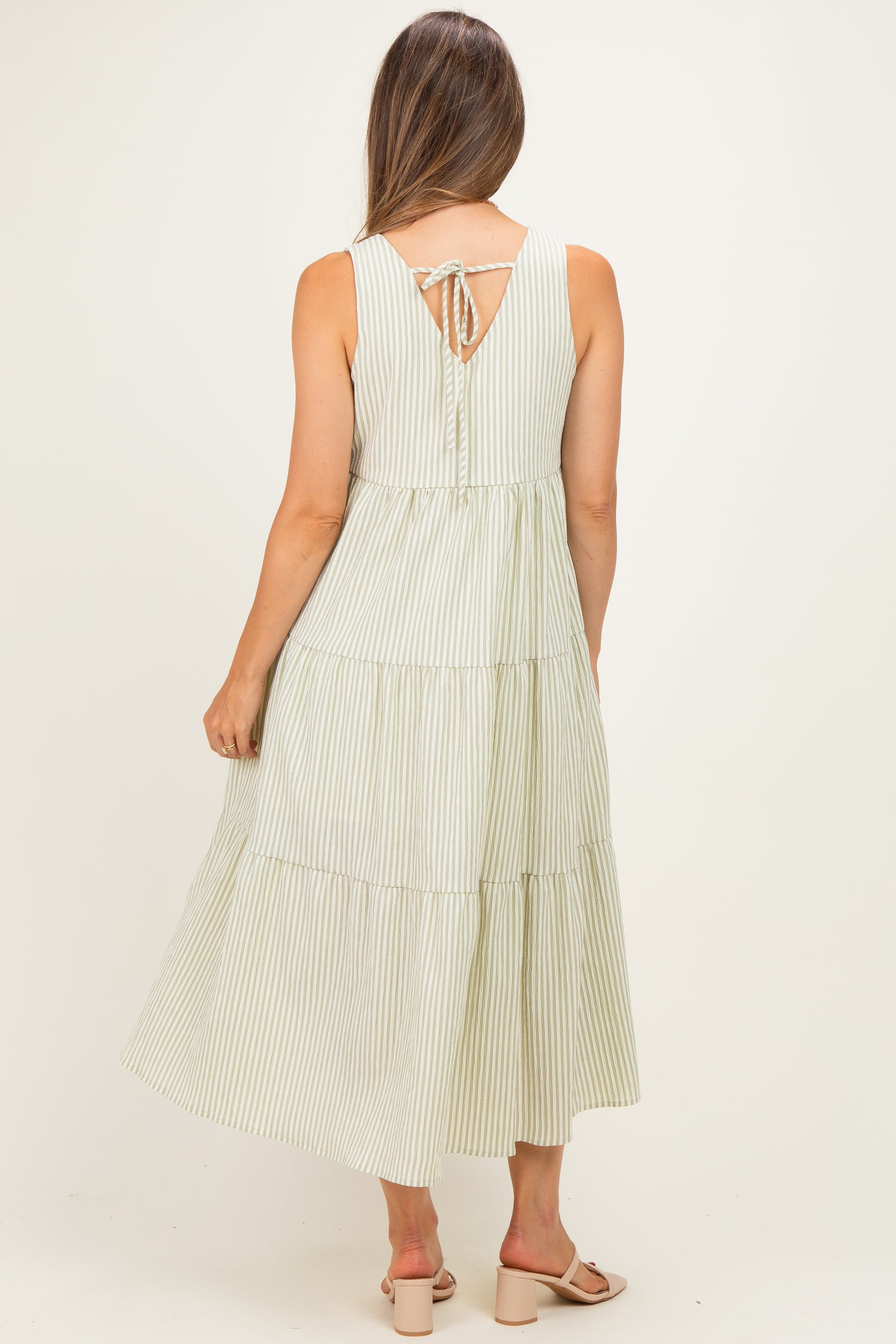 woman wearing a green and white striped maternity dress with a tiered skirt and tie detail at the back
