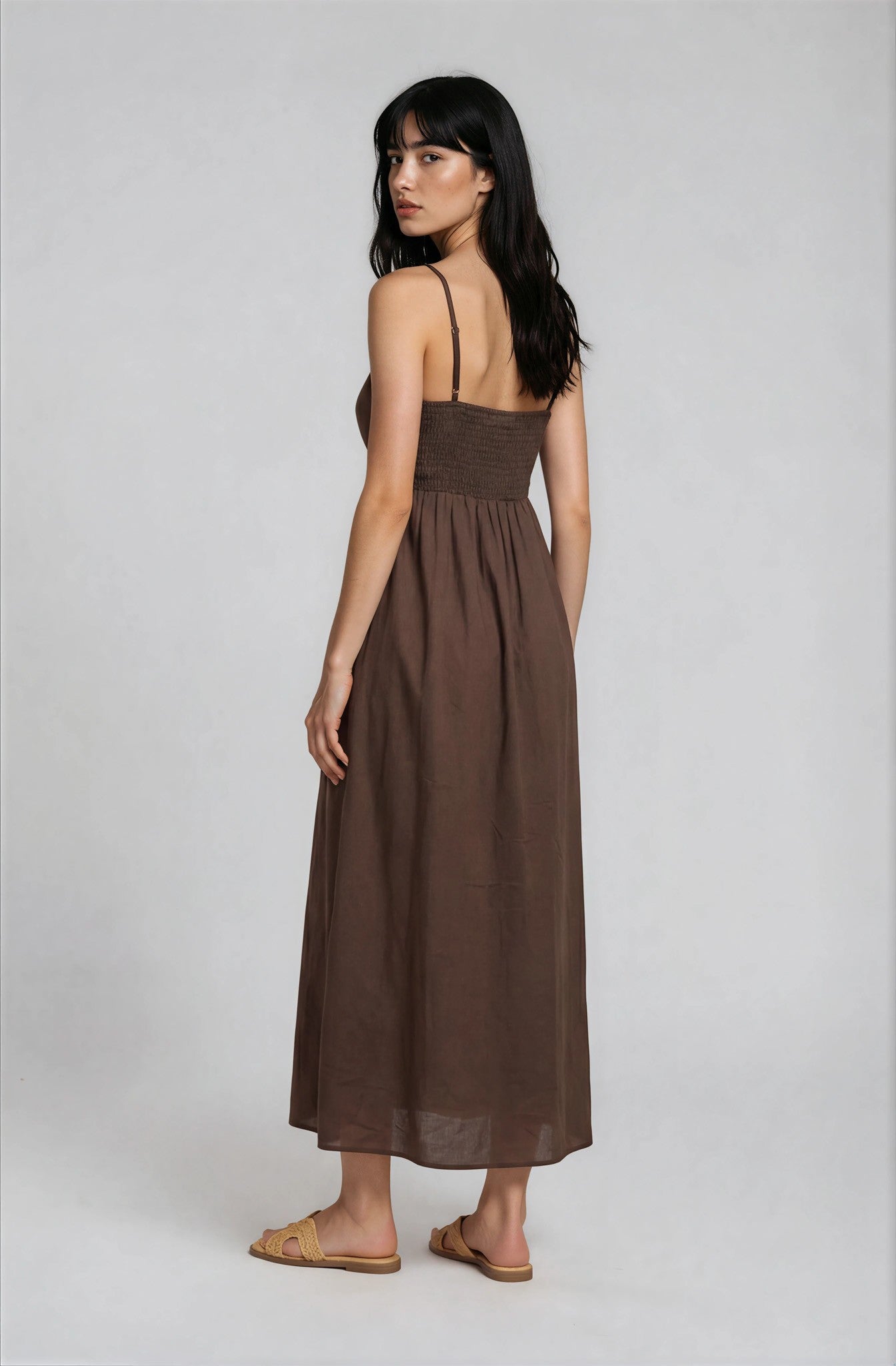 woman wearing a brown maxi dress with a smocked bodice and spaghetti straps, viewed from the back