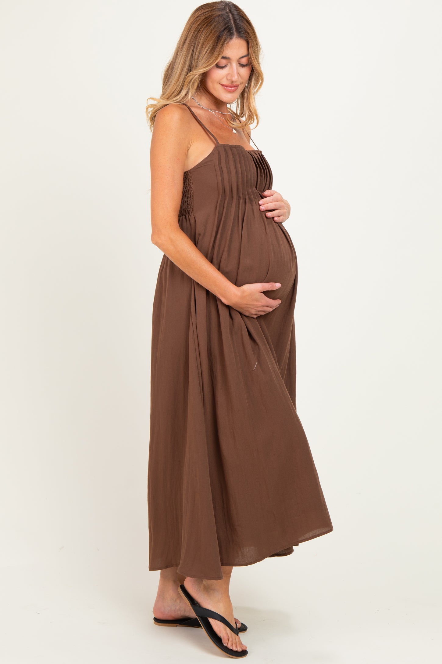 woman wearing a brown maxi maternity dress with smocked bodice, cradling her baby bump