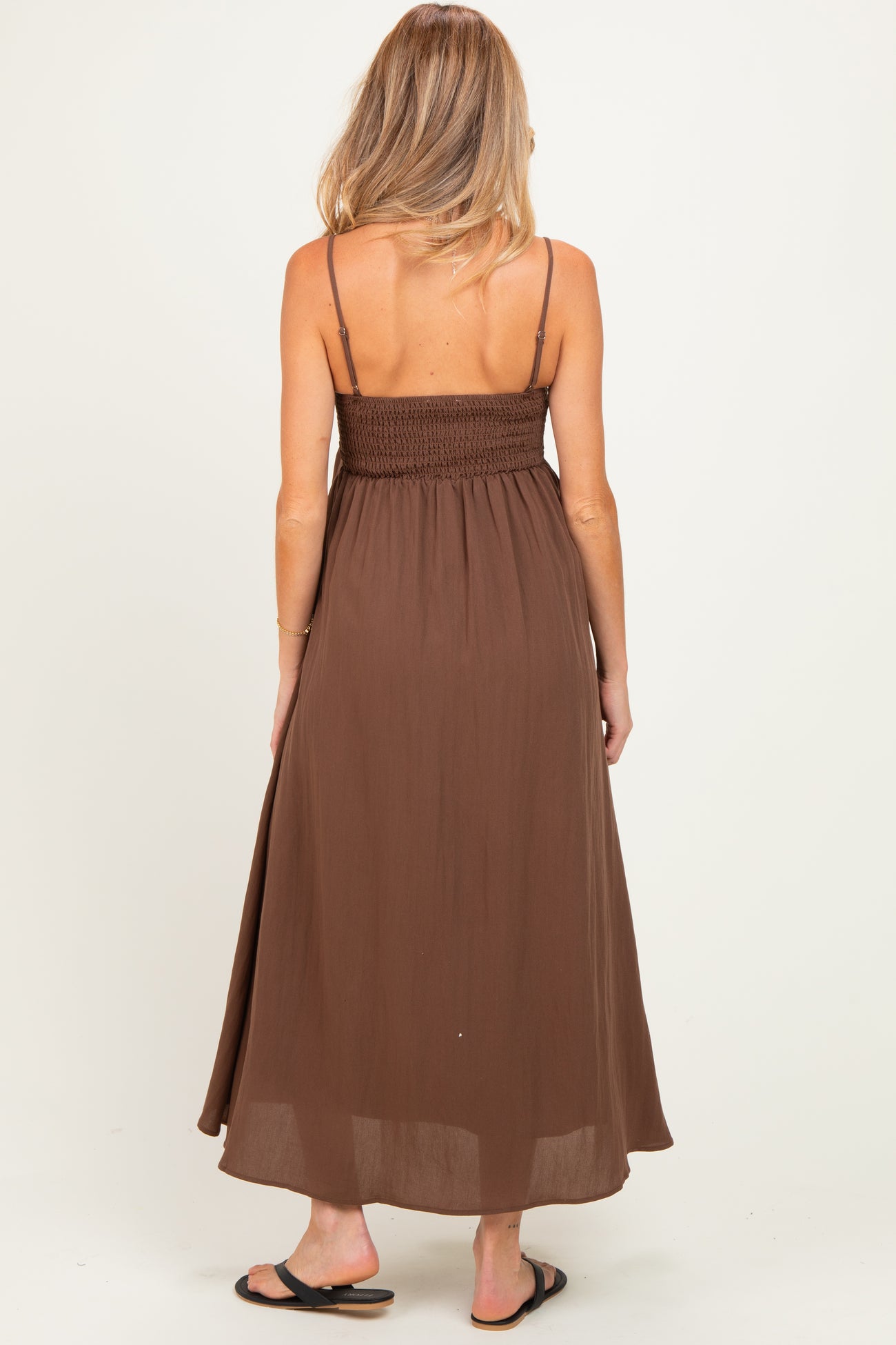 woman wearing a brown maternity maxi dress with a smocked back and thin straps, showing off her baby bump