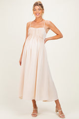 woman wearing a light peach maternity maxi dress with pleated bodice and spaghetti straps, showing her baby bump