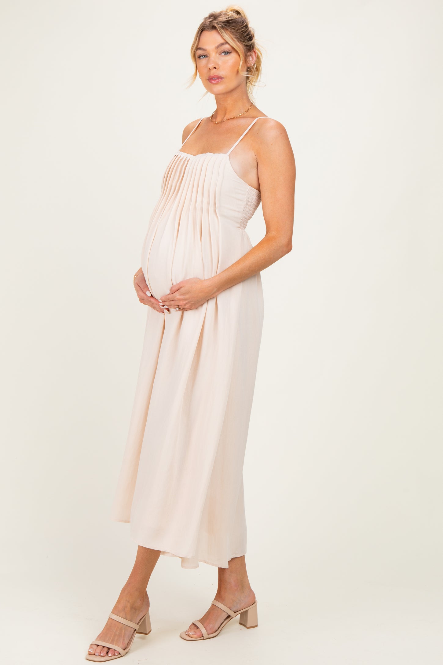 woman wearing a light pink maternity dress with pleated detailing and holding her baby bump