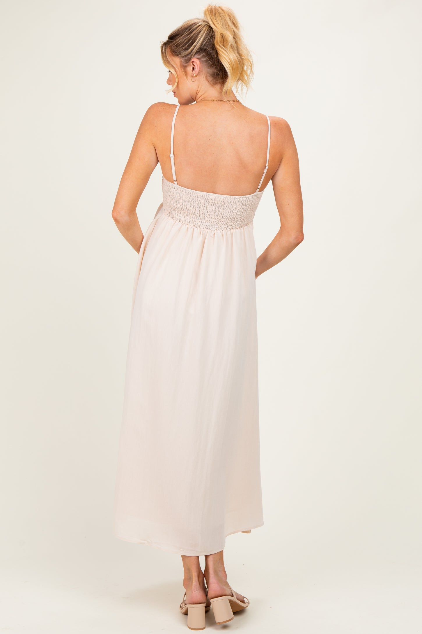 woman wearing a light pink maternity dress with smocked back and spaghetti straps, showing her baby bump from the back