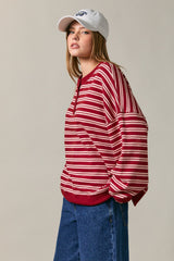 woman wearing a red and white striped oversized sweater with a round neckline and blue jeans, accessorized with a white baseball cap