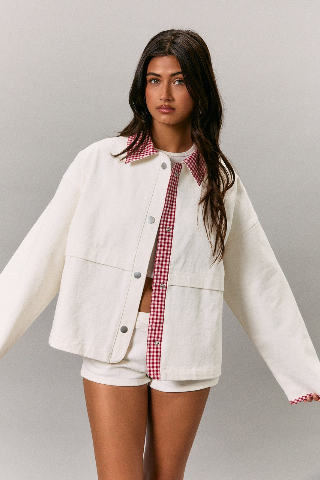woman wearing a white oversized jacket with a red gingham collar and short white shorts
