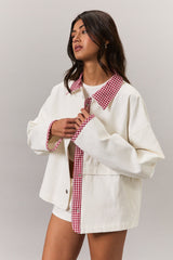 woman wearing an oversized white denim jacket with a red gingham collar and cuffs, styled casually