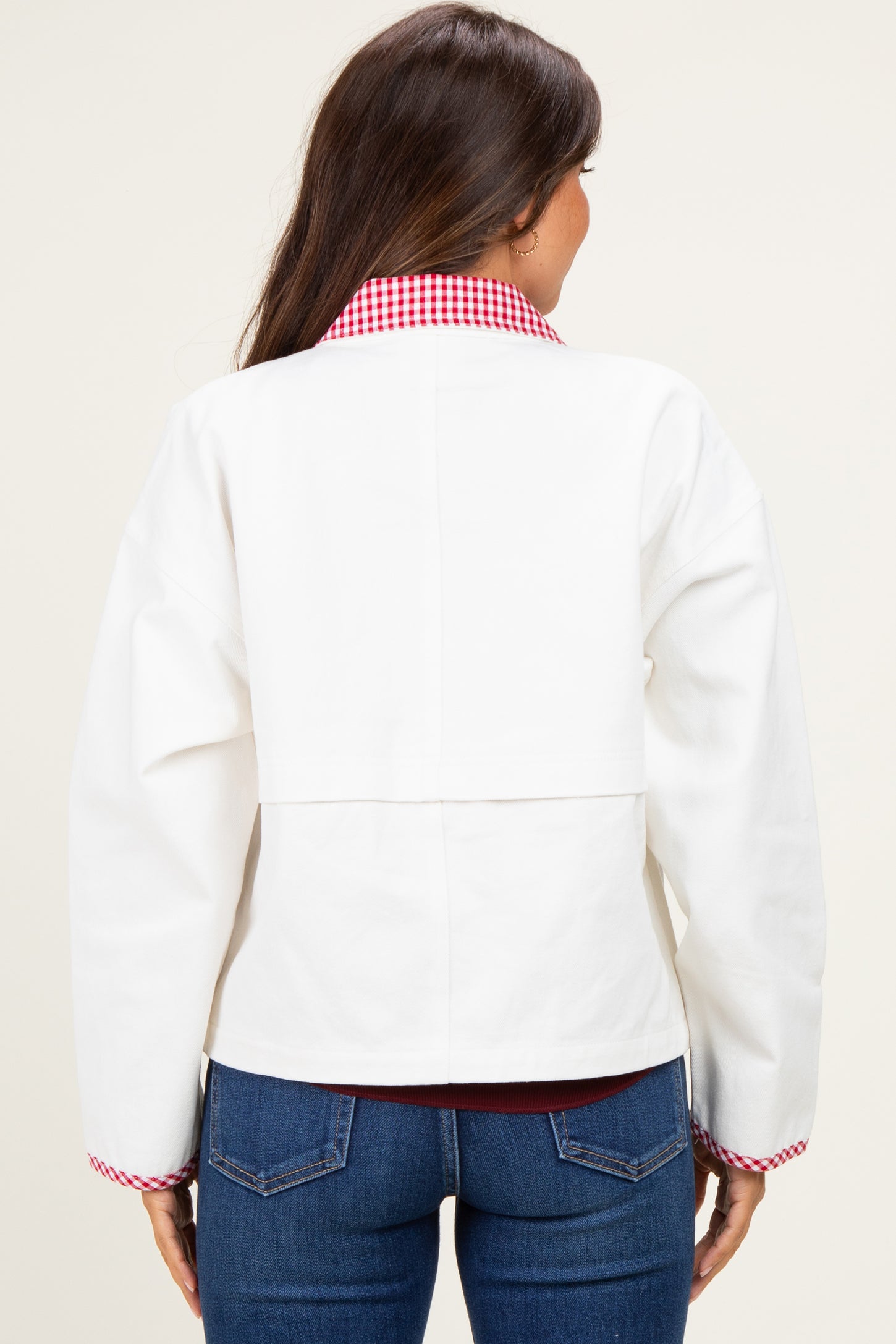 woman wearing a white maternity jacket with a red gingham collar and back detail, styled with blue jeans