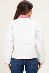 woman wearing a white maternity jacket with a red gingham collar and back detail, styled with blue jeans