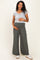 woman wearing a gray maternity top and olive green wide leg pants, holding her baby bump