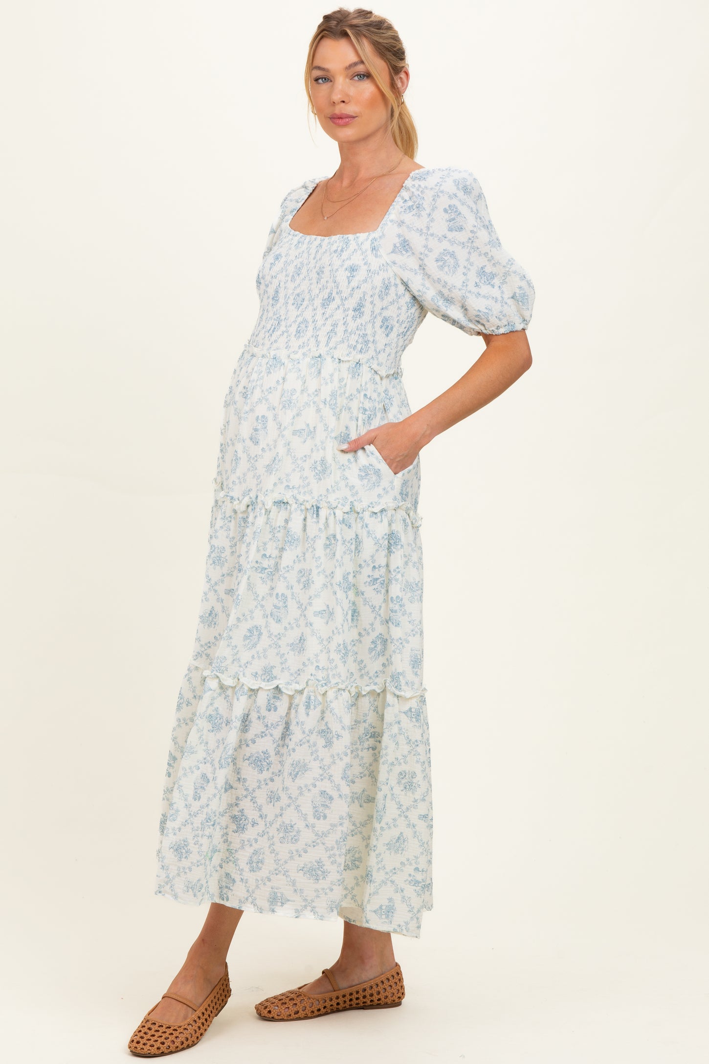 woman wearing a light blue floral print maternity dress with a square neckline and tiered skirt, showing her baby bump