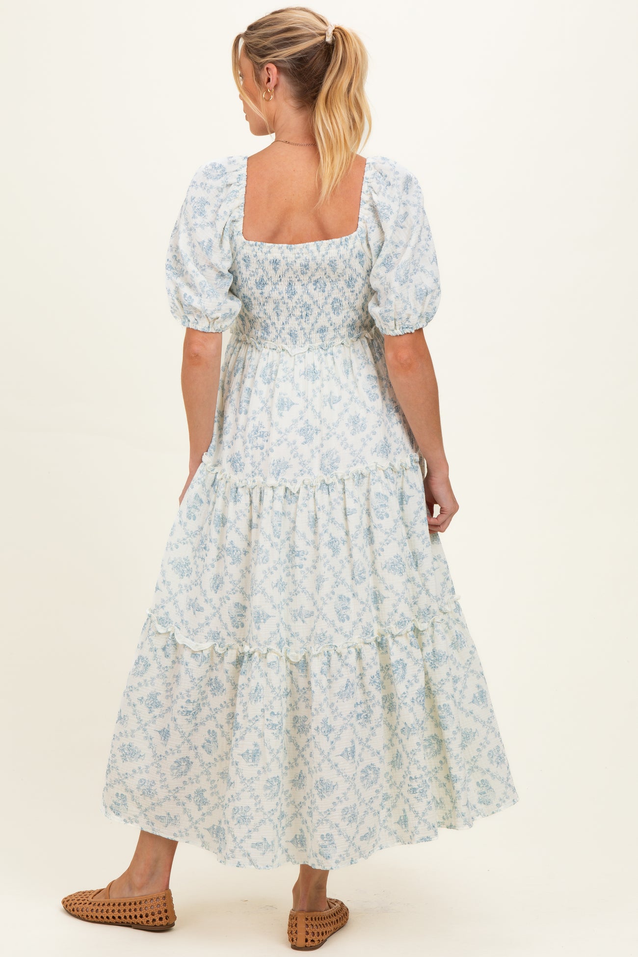 woman wearing a light blue floral maternity dress with puff sleeves and a tiered skirt, showing a baby bump from behind