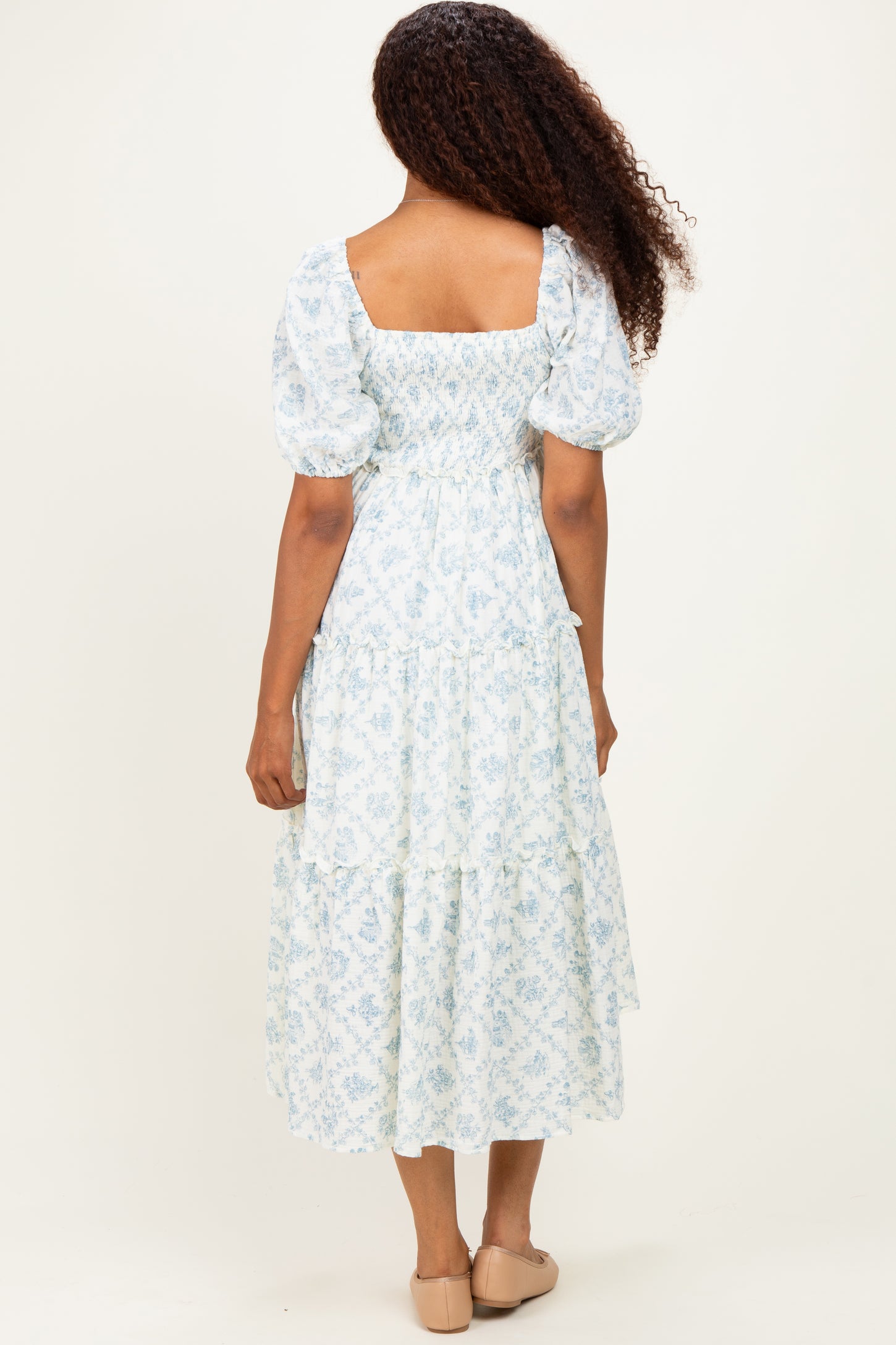 woman wearing a light blue floral tiered maxi dress with puff sleeves and a square neckline, seen from the back