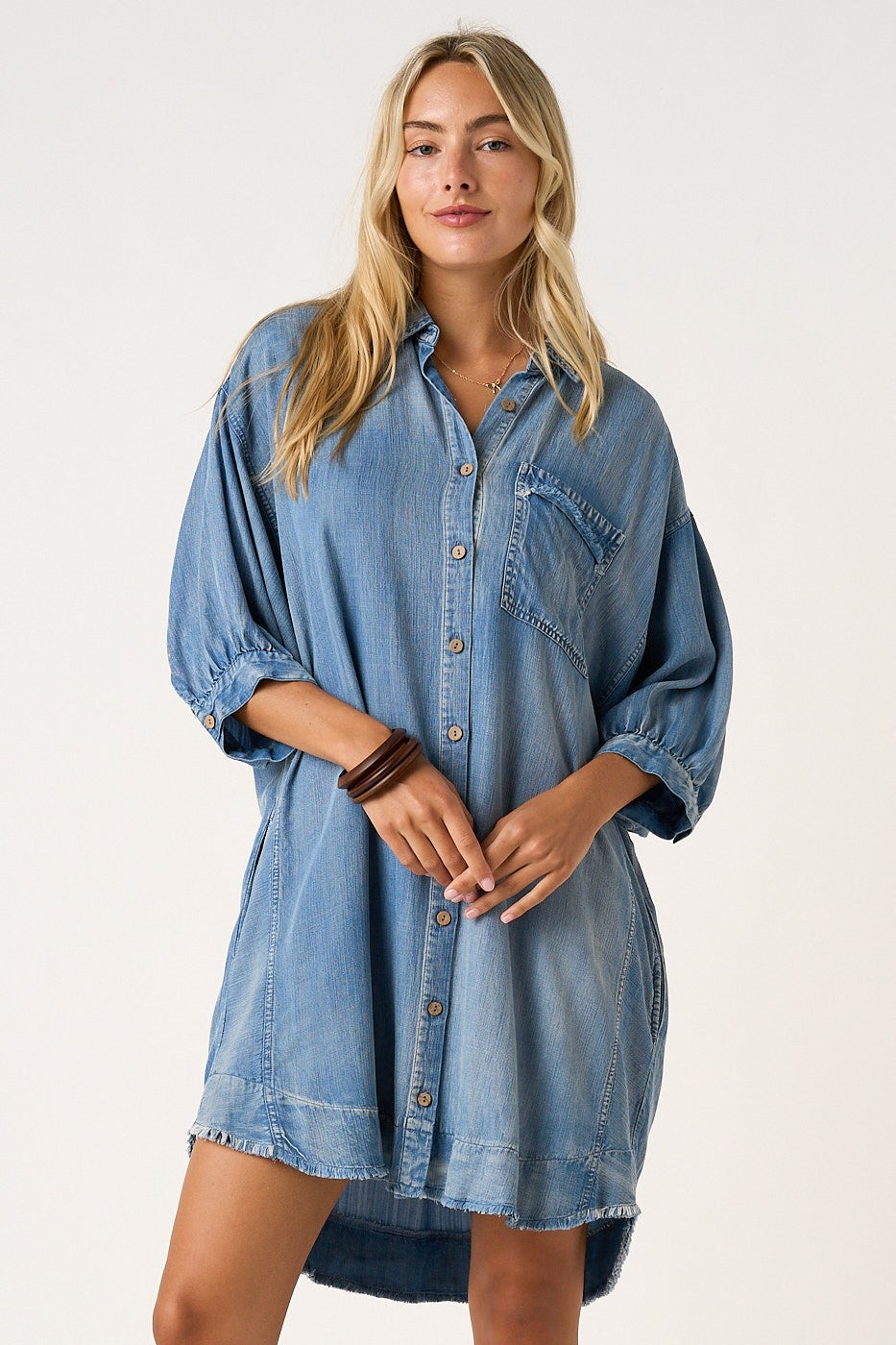 woman wearing a light blue oversized denim shirt dress with button closure and a chest pocket