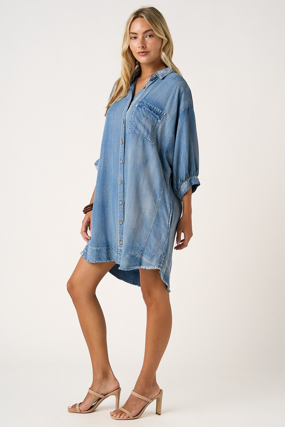 woman wearing a light blue denim shirt dress with a front pocket and rolled sleeves, standing in a relaxed pose