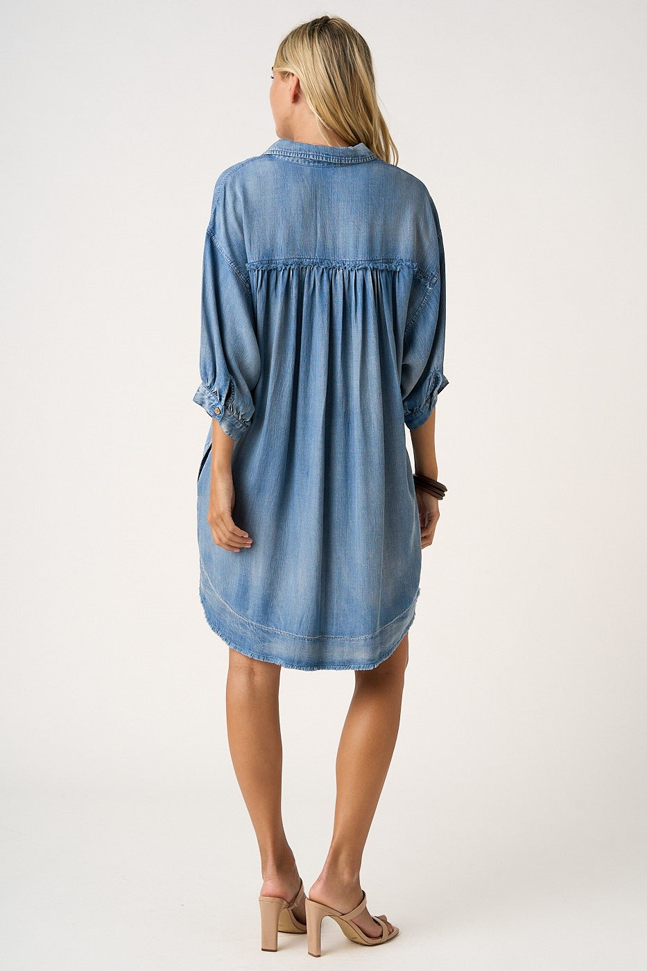 woman wearing a loose-fitting light blue denim dress with three-quarter sleeves and a gathered back detail