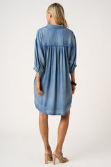 woman wearing a loose-fitting light blue denim dress with three-quarter sleeves and a gathered back detail
