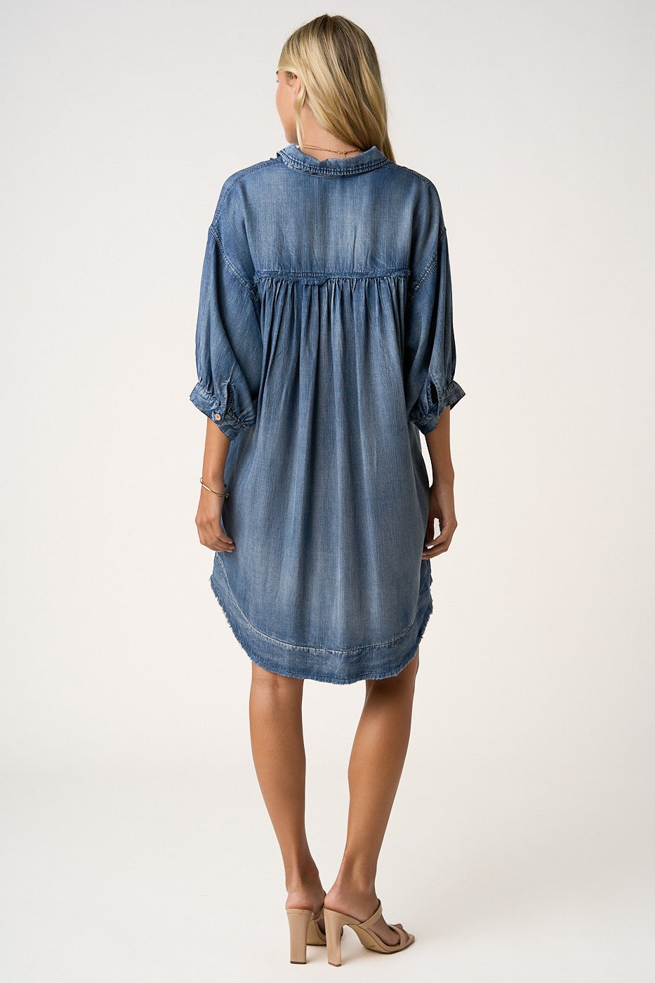 woman wearing a denim chambray shirt dress with three-quarter sleeves and a relaxed fit, shown from the back