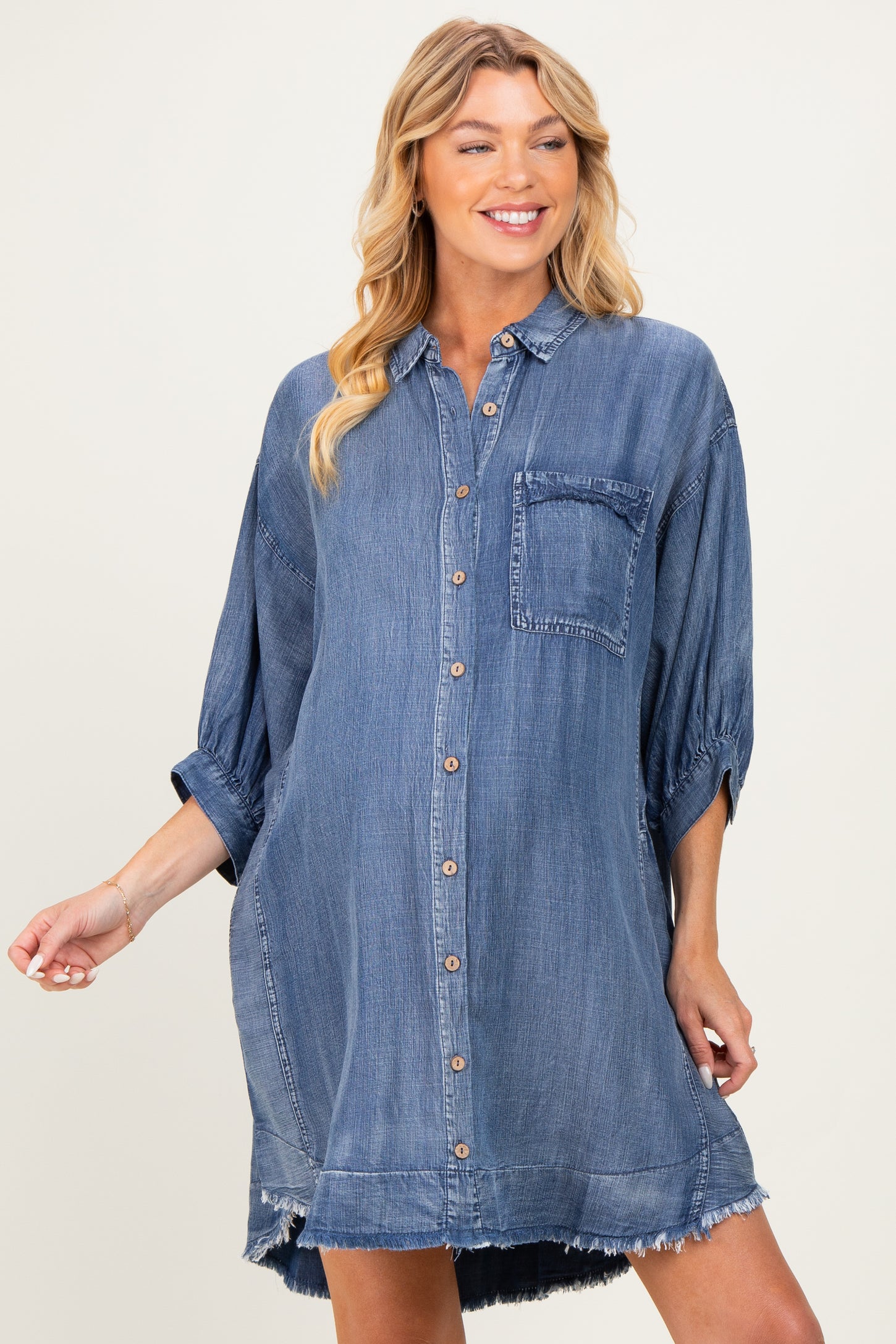 woman wearing a blue denim maternity shirt dress with a button-down front and rolled sleeves, featuring a pocket and frayed hem