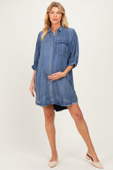 woman wearing a maternity denim shirt dress with a button front and rolled sleeves, gently holding her baby bump