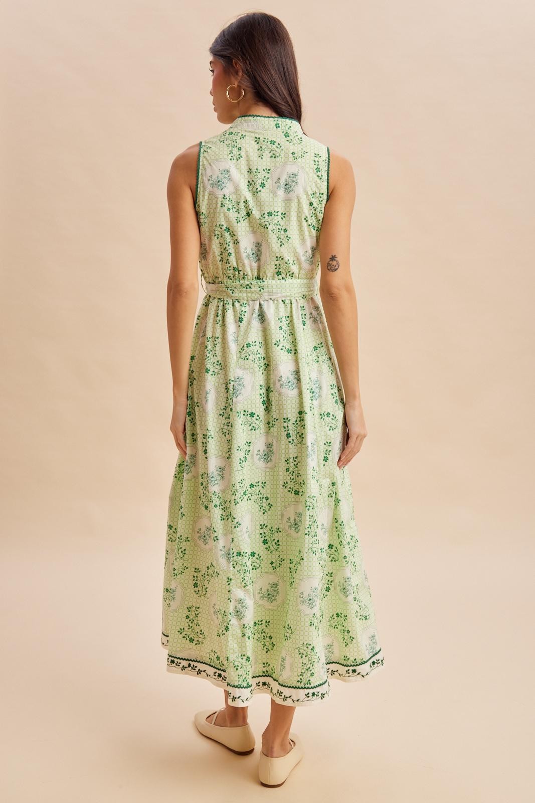 woman wearing a green sleeveless maxi dress with a floral pattern and a belted waist, viewed from the back