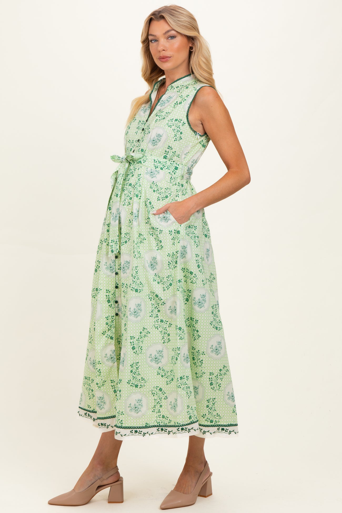 woman wearing a green floral print maternity dress with a collar, sleeveless design, and pockets