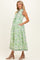 woman wearing a green floral print maternity dress with a collar, sleeveless design, and pockets