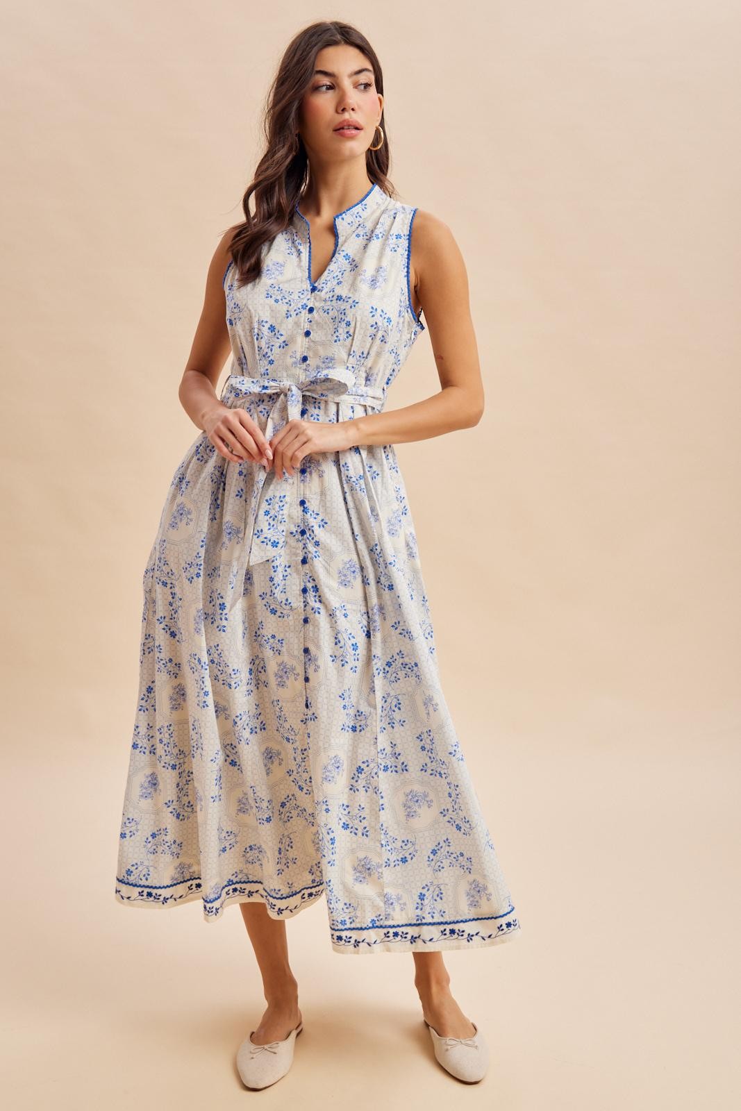 woman wearing a sleeveless light blue floral midi dress with a cinched waist and a belted detail