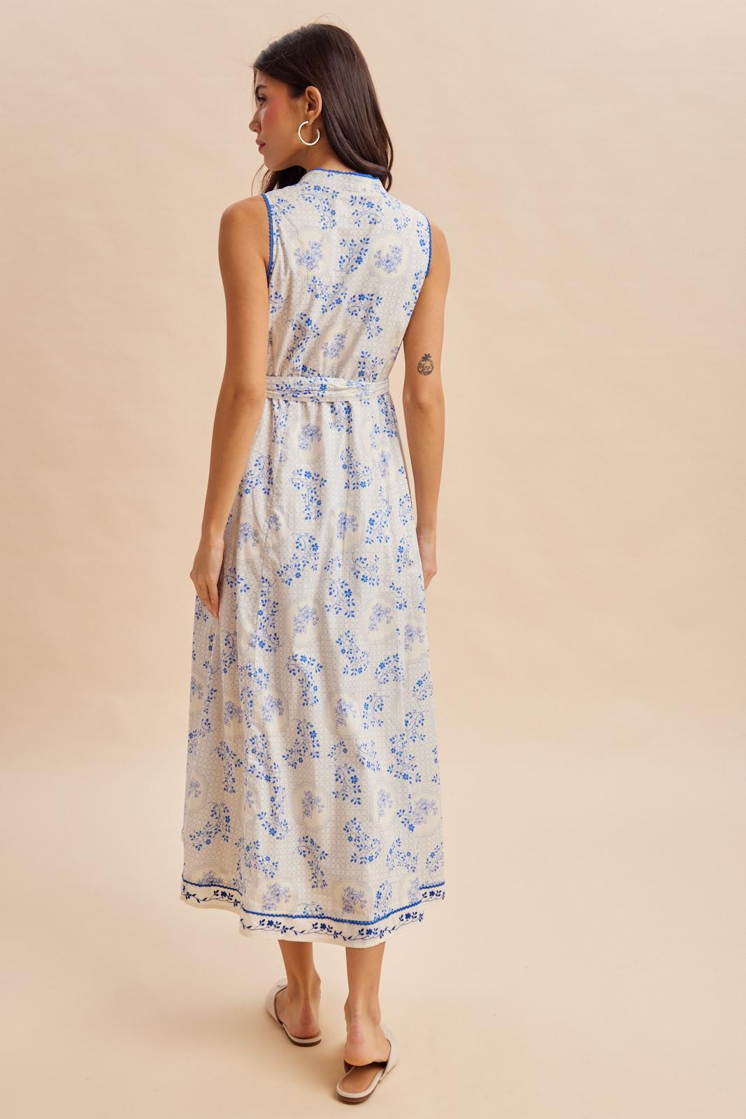 woman wearing a sleeveless maxi dress with a floral print in blue and cream, viewed from the back
