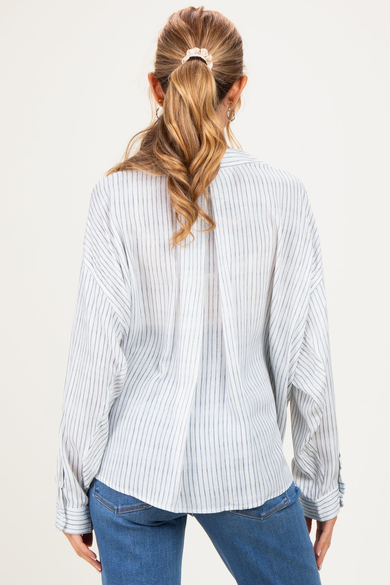 woman wearing a light blue striped maternity top with long sleeves, seen from the back, paired with blue jeans