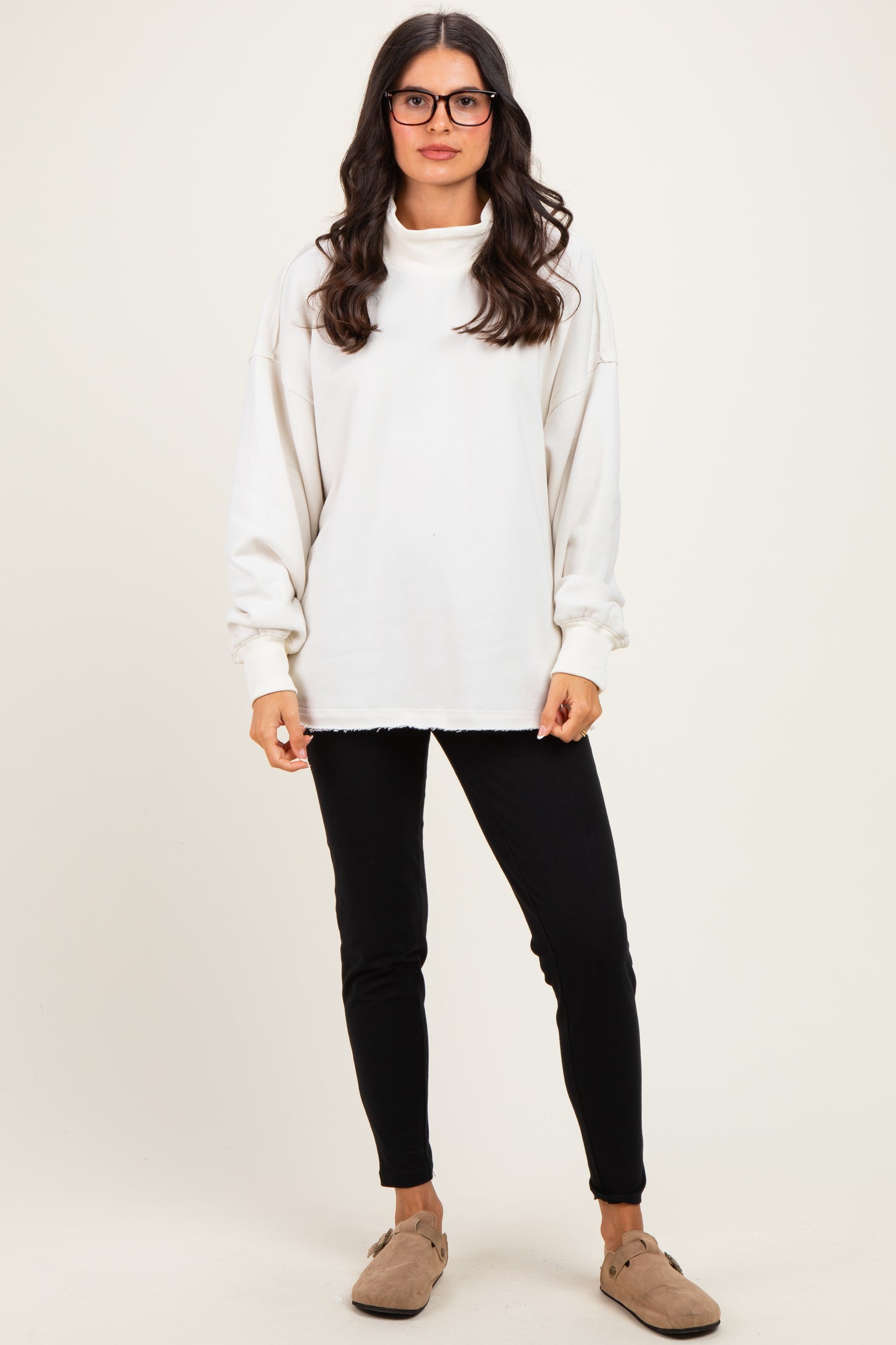 woman wearing a white oversized sweatshirt with a cowl neck and black skinny pants
