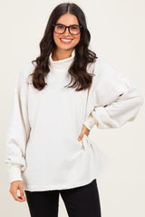 woman wearing an oversized cream turtleneck sweatshirt with long sleeves and a curved hem, paired with black pants