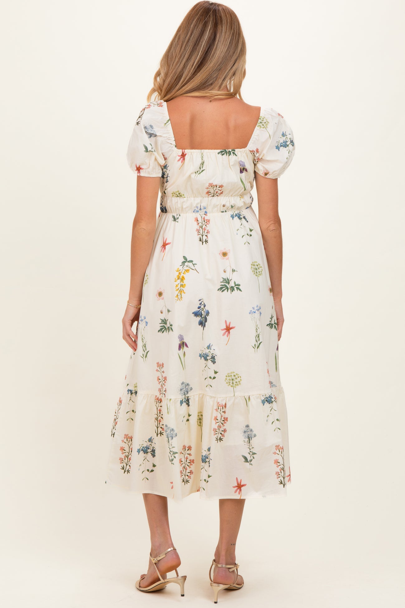 woman wearing a floral print maternity dress with puff sleeves and a tiered hem, showing a baby bump from the back