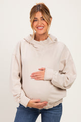woman wearing a beige maternity hoodie with a ruffled hem, cradling her baby bump
