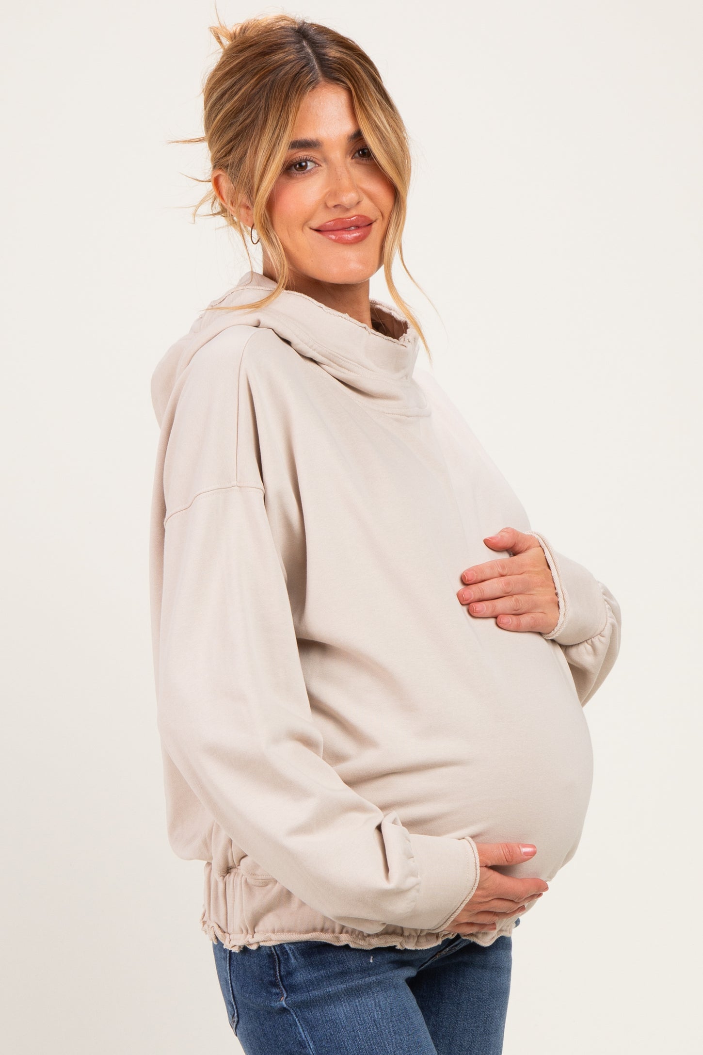 woman wearing a beige maternity hoodie, highlighting her baby bump with a relaxed fit and gathered hem