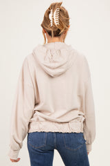 woman wearing a beige maternity hoodie with a cinched waist and hood, seen from the back