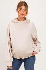 woman wearing a light beige maternity hoodie with a ruffled hem and a visible baby bump, paired with jeans