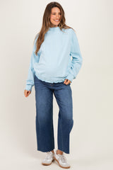 woman wearing a light blue maternity sweatshirt with a high neckline and wide leg jeans, showing her baby bump