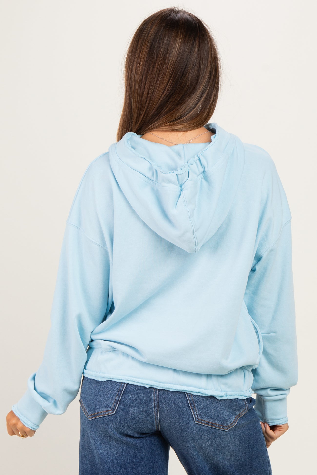 woman wearing a light blue oversized maternity hoodie, with a relaxed fit and adjustable hood, seen from the back