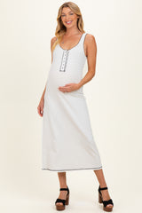 woman wearing a white maternity maxi dress with a decorative neckline and holding her baby bump
