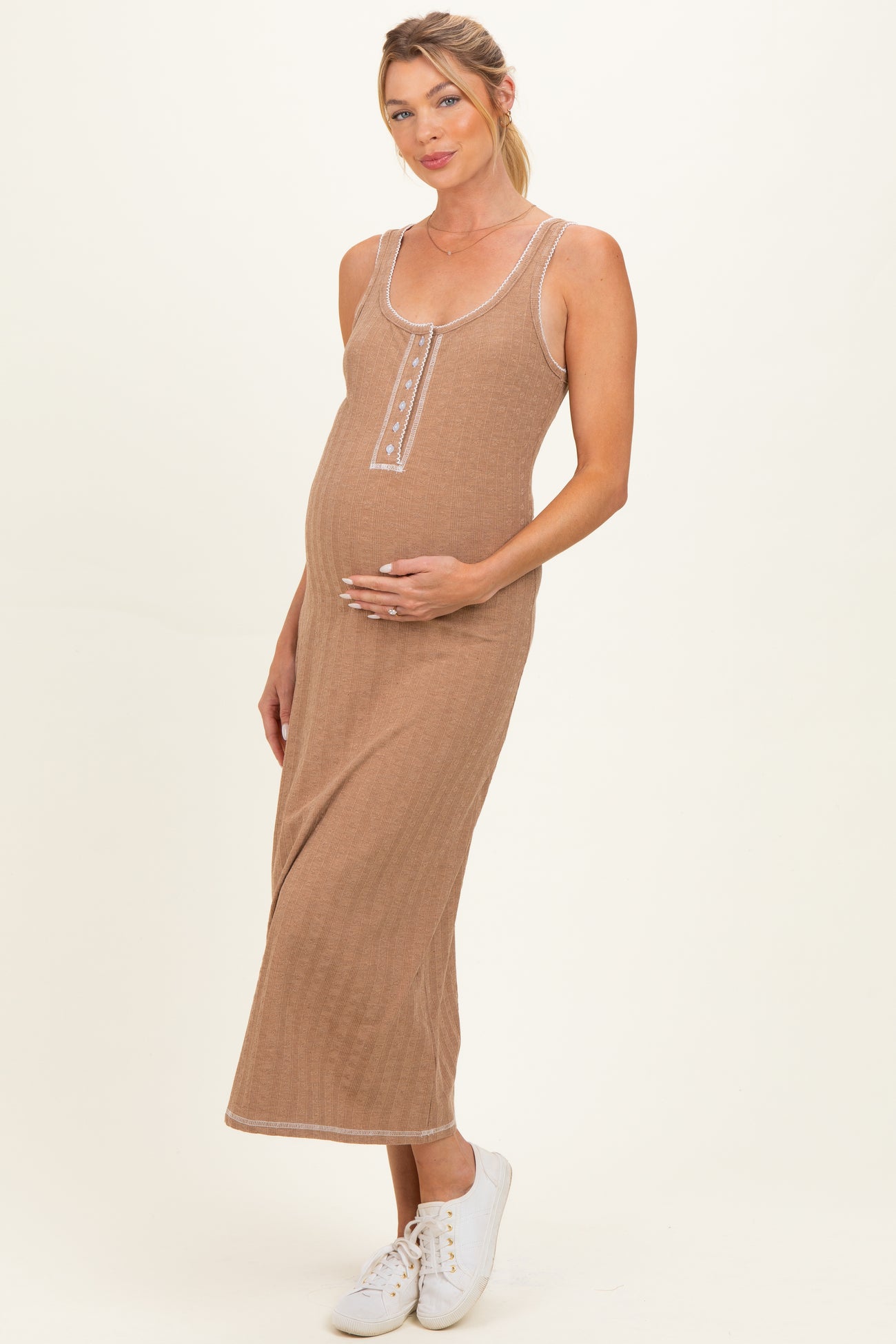 woman wearing a brown ribbed maternity dress with buttons, gently holding her baby bump