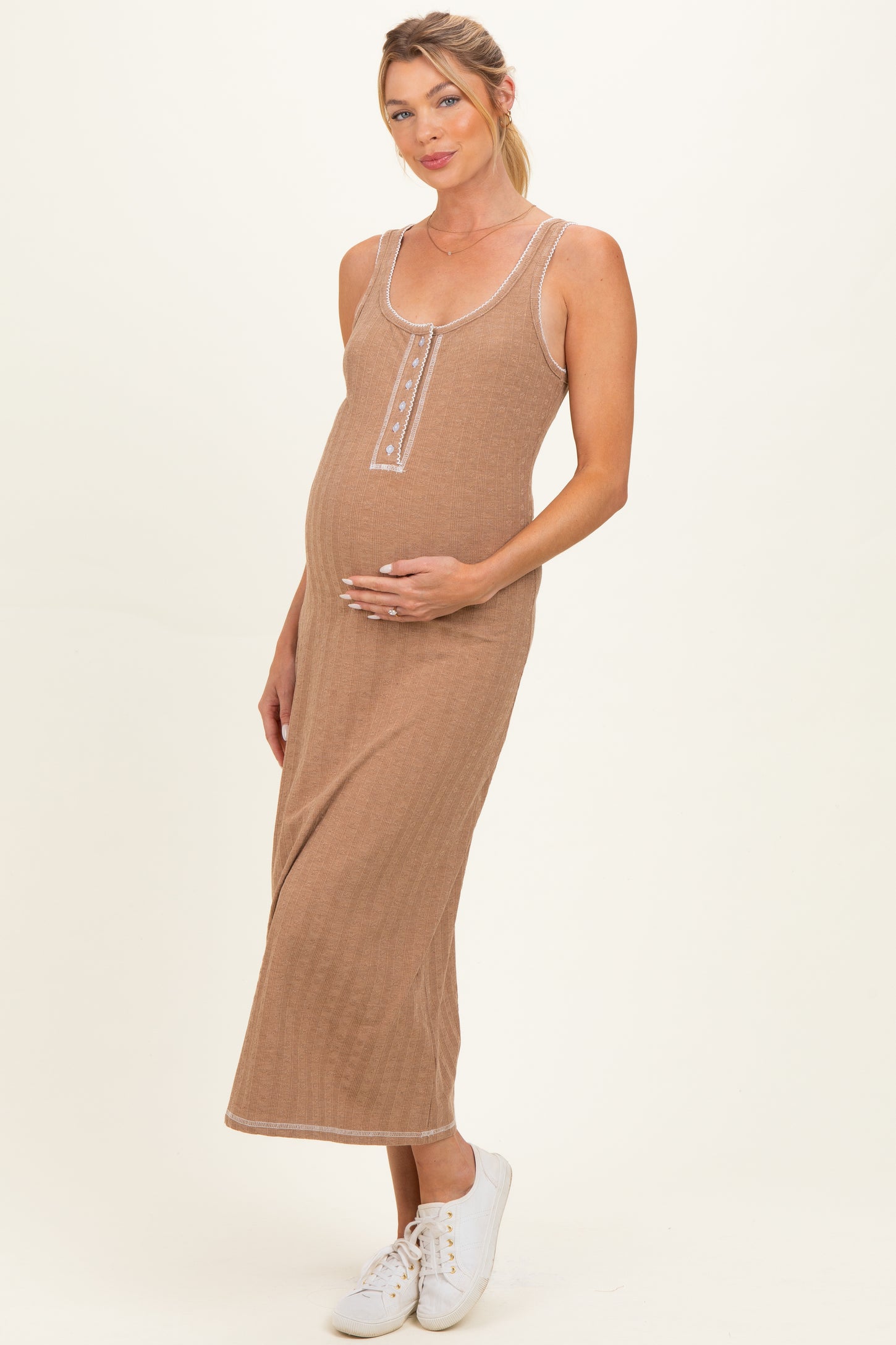 woman wearing a brown ribbed maternity dress with buttons, gently holding her baby bump