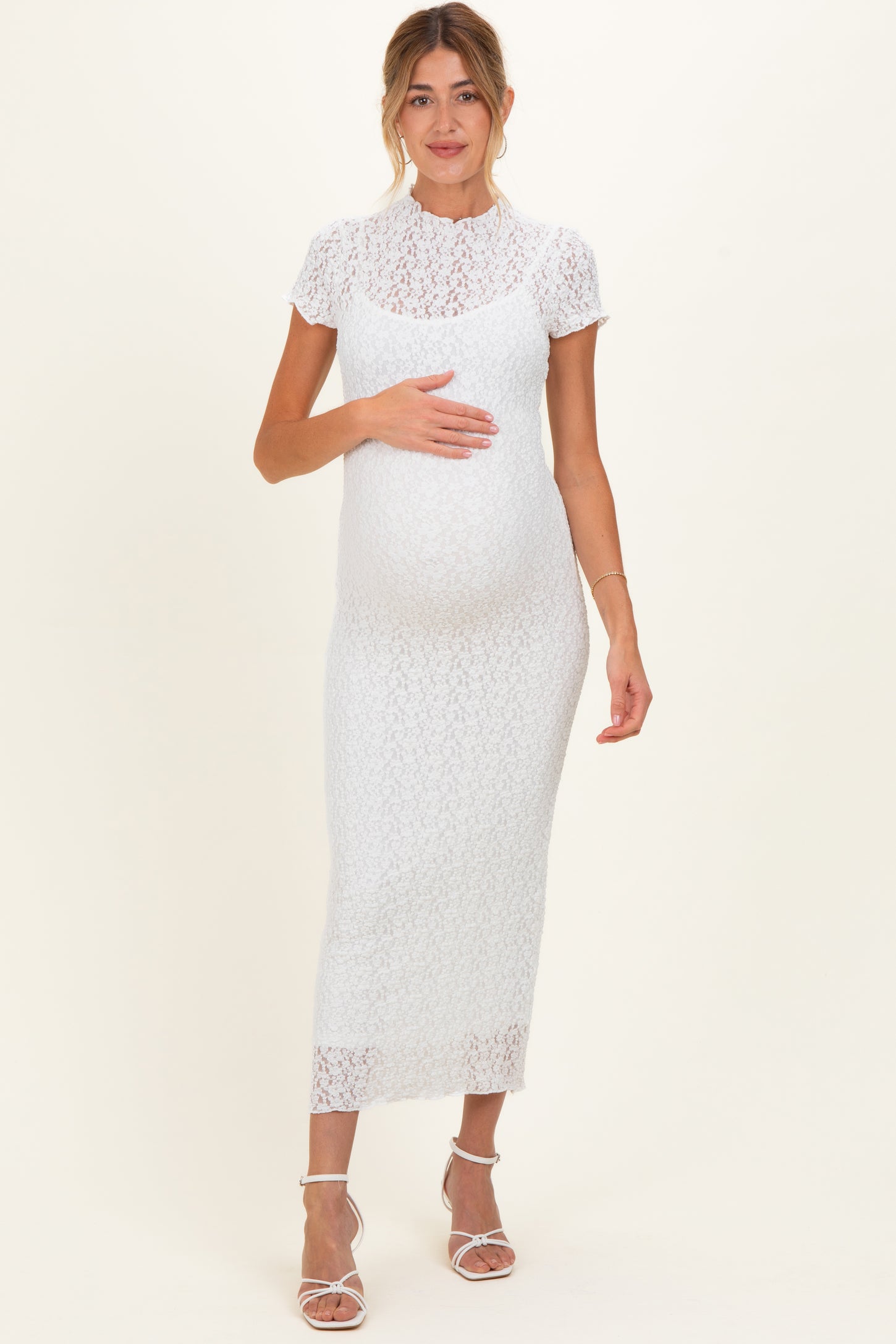 woman wearing a white lace maternity dress and holding her baby bump