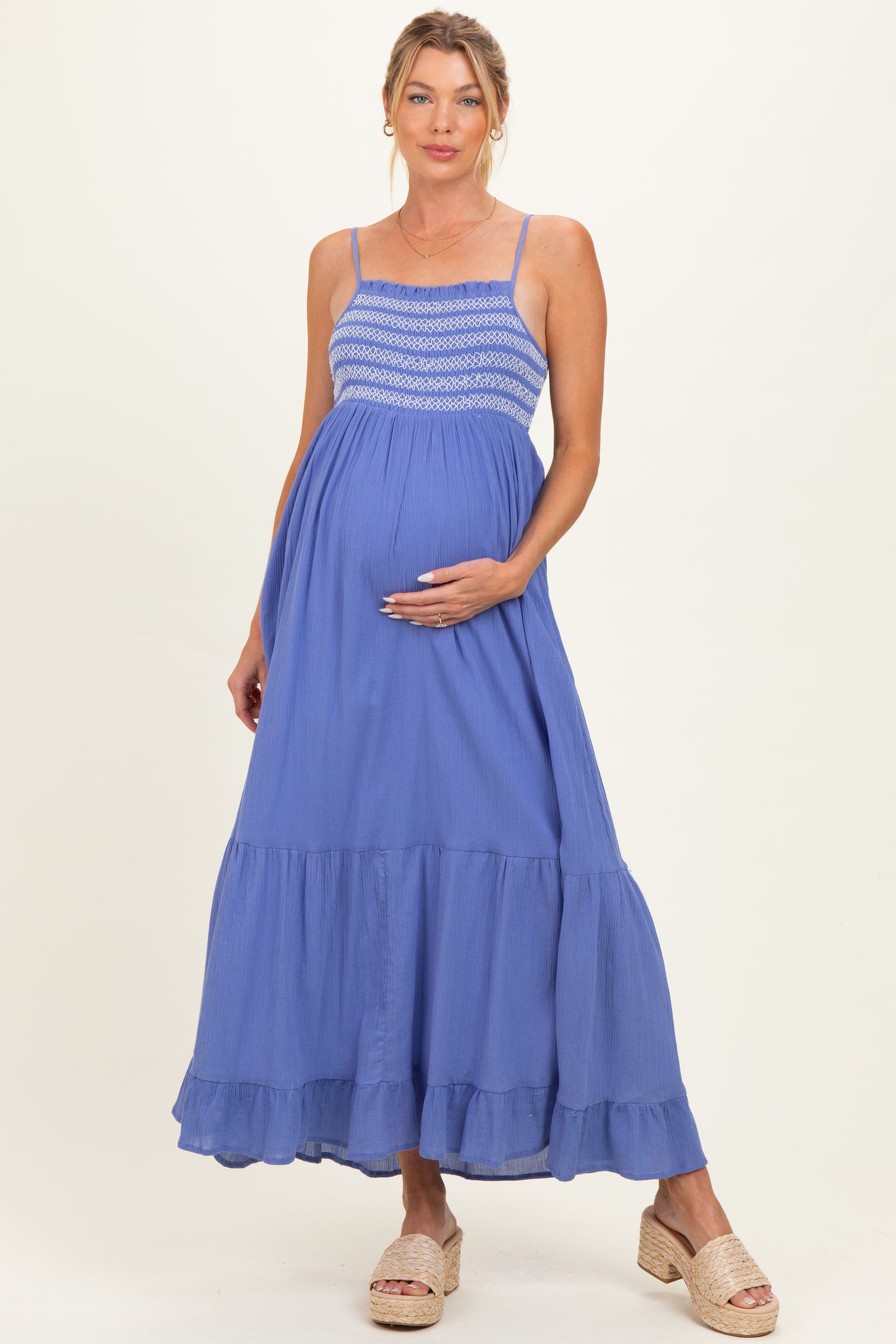 woman wearing a blue maternity maxi dress with a smocked bodice and ruffled hem, holding her baby bump